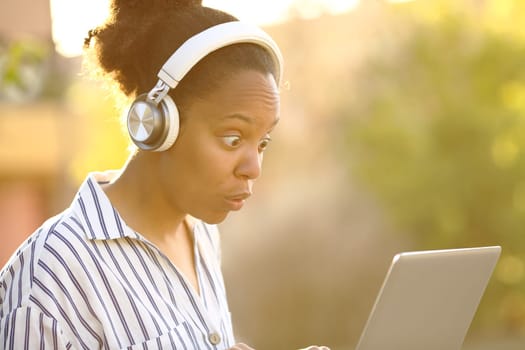 Surprised black woman watching media on laptop in a park