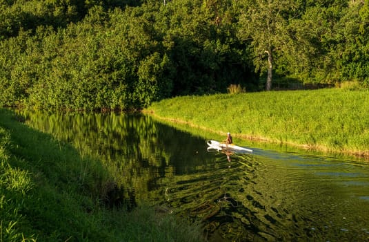 A man paddles a traditional Hawaiian outrigger canoe through the tranquil waters of Hanalei River on a sunny day, creating mirrored reflections.