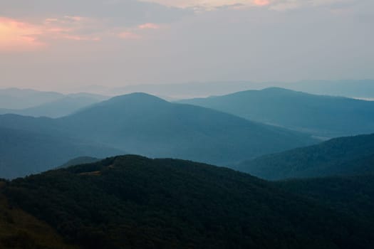 Sunset in mountains. Natural mountain landscape with illuminated misty peaks, foggy slopes and valleys, blue sky with orange yellow sunlight. Amazing scene from Bieszczady Mountains in Poland