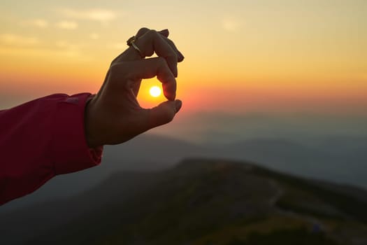 Sun over female hand. Sunrise in mountains. Ready for adventure. Natural mountain landscape with illuminated misty peaks, foggy slopes and valleys, blue sky with orange yellow sunlight