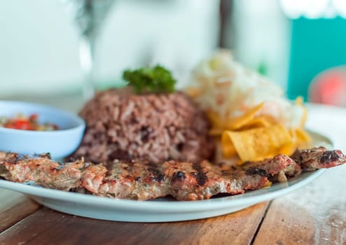 Close up of roast beef with gallo pinto and pico de gallo, Nicaraguan food served on wooden table, Plate with roast beef and rice served on wooden table