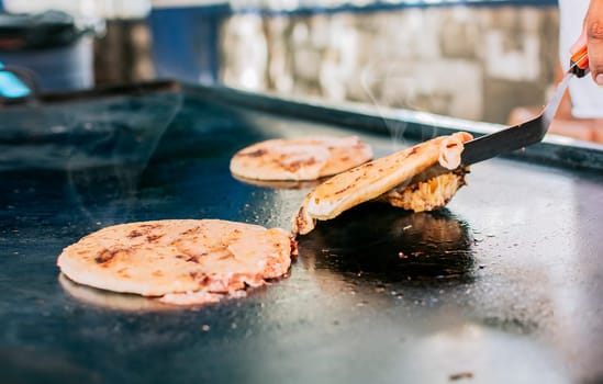 Spatula taking a traditional cheese pupusas on the grill, Close up of traditional artisan grilled pupusas. Traditional Nicaraguan pupusas with melted grilled cheese