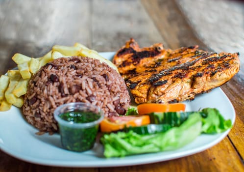 Close up of roasted chicken with gallo pinto and salad served on table, Plate with roast chicken and rice served on wooden background. Nicaraguan food served on wooden background