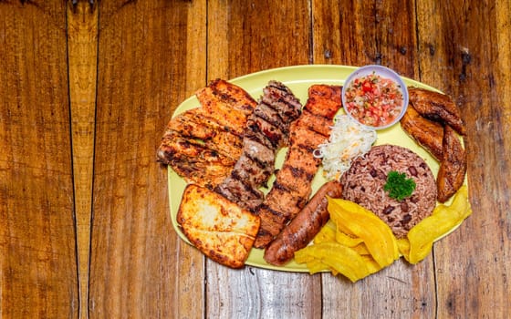 Varieties of grilled meats with rice, fried cheese and tomato salad, plate with assorted types of grilled meats on wooden table, traditional Nicaraguan food served on wooden table