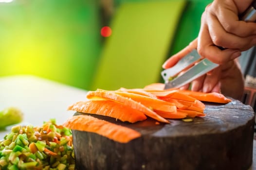 Close up of hands cutting pieces of carrot on homemade wooden base , Hands cutting carrot on homemade log with copy space