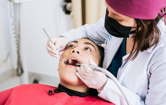 Female dentist cleaning and examining a female patient mouth. Dental specialist cleaning the teeth of a female patient. Professional dentist cleaning a female patient's mouth