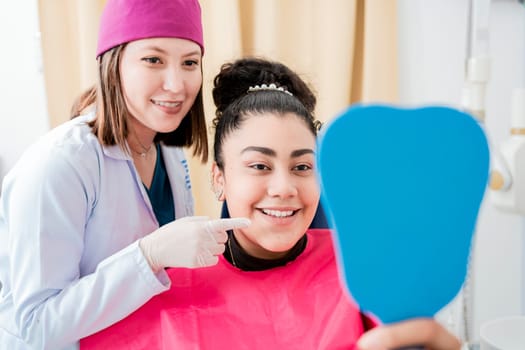 Dentist with satisfied patient smiling at dental mirror, Satisfied patient in dental clinic looking at mirror, female patient checking teeth after curing teeth in dental clinic.
