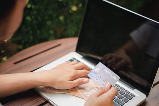 Hands of businesswoman holding thai money and credit card on laptop computer, woman using working and shopping, Online e-commerce, internet banking