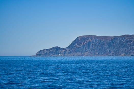 View from the sea to the West Cape in Norway in sunshine. Waves in the foreground, rocks in the background. Westernmost point of Europe mainland.