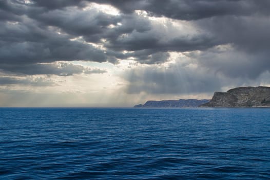 View from the sea to the West Cape in Norway in sunshine with heavy clouds. Waves in the foreground, rocks in the background. Westernmost point of Europe mainland.