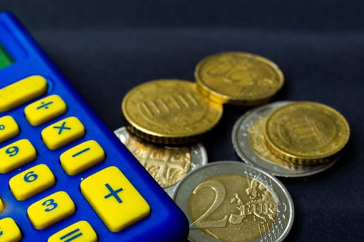 Money concept. Blue calculator with coins euro, close up, dark black background