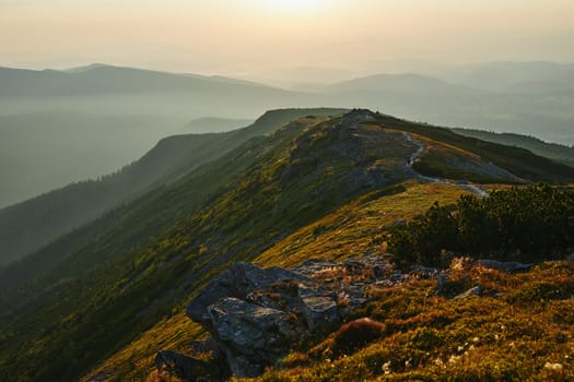 Sunrise in mountains. Natural mountain landscape with illuminated misty peaks, foggy slopes and valleys, blue sky with orange yellow sunlight. Amazing scene from Beskid Zywiecki in Poland