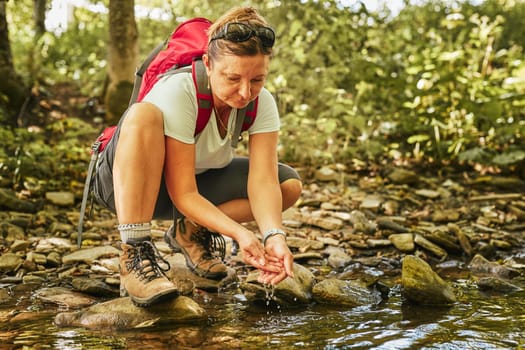 Traveling trekking with backpack concept image. Backpacker female in trekking boots crossing mountain river. Woman hiking in mountains during summer trip. Vacation trip close to nature. Natural scenery