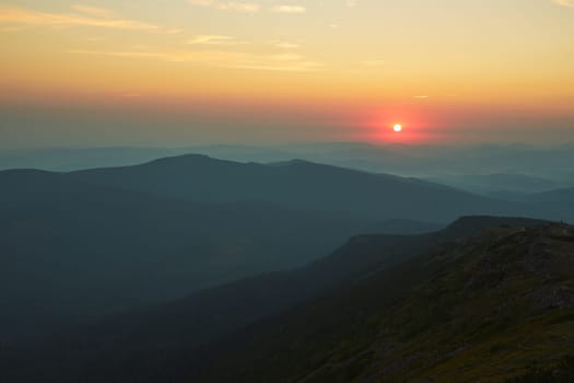 Sunrise in mountains. Natural mountain landscape with illuminated misty peaks, foggy slopes and valleys, blue sky with orange yellow sunlight. Amazing scene from Beskid Zywiecki in Poland