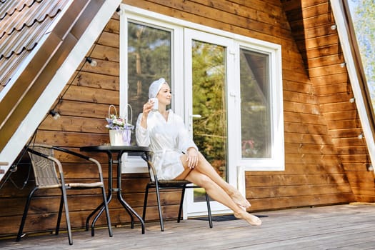 Relaxed woman in bathrobe enjoying morning coffee on terrace of tiny house. Concept of renting of a bungalow to retreat