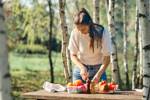 Woman makes vegetable salad outdoor at picnic in sunny day