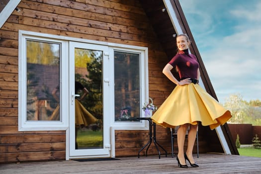 Cheerful woman in long waving skirt and purple pullover dancing on terrace of a-frame cabin
