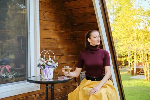 Confident woman in sitting on veranda of wooden summer house. Concept of countryside summer vacation.