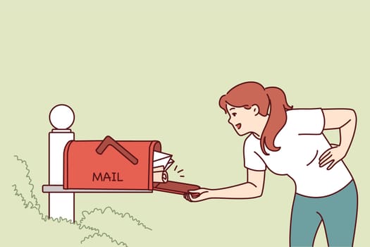 Woman checks street mailbox filled with envelopes and parcels, hoping to receive long-awaited letter. Girl looks into mailbox with smile and rejoices at abundance of letters from friends