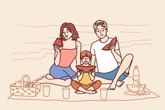 Family sitting on seashore, eating watermelon and relaxing on sunny beach in hot summer weather. Young family of boy and parents had picnic on tropical island during trip to resort