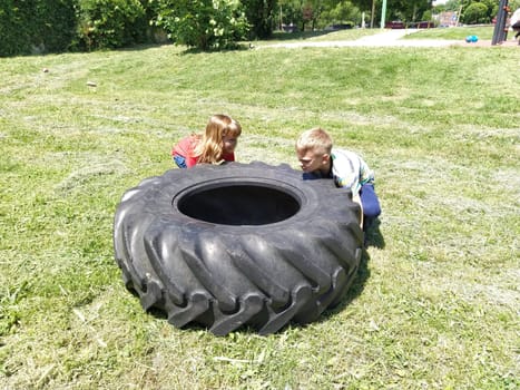 Sremska Mitrovica, Serbia, May 20, 2020. Children play and pick up the tire. Car parts and accessories in a kid's game. A boy and a girl 6 and 7 years old are doing strength exercises on the grass.