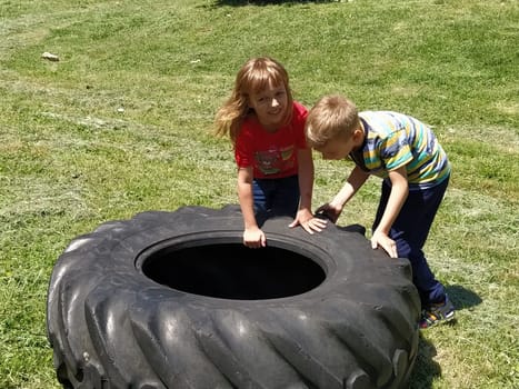 Sremska Mitrovica, Serbia, May 20, 2020. Children play and pick up the tire. Car parts and accessories in a kid's game. A boy and a girl 6 and 7 years old are doing strength exercises on the grass.