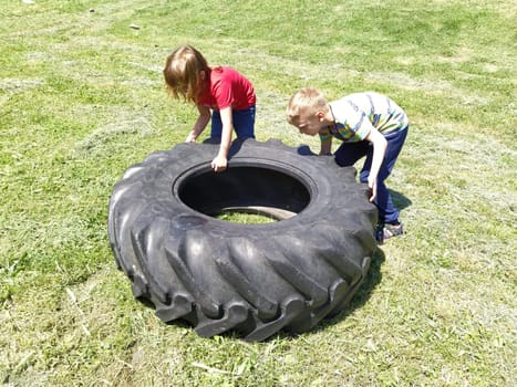 Sremska Mitrovica, Serbia, May 20, 2020. Children play and pick up the tire. Car parts and accessories in a kid's game. A boy and a girl 6 and 7 years old are doing strength exercises on the grass.