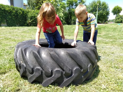 Sremska Mitrovica, Serbia, May 20, 2020. Children play and pick up the tire. Car parts and accessories in a kid's game. A boy and a girl 6 and 7 years old are doing strength exercises on the grass.
