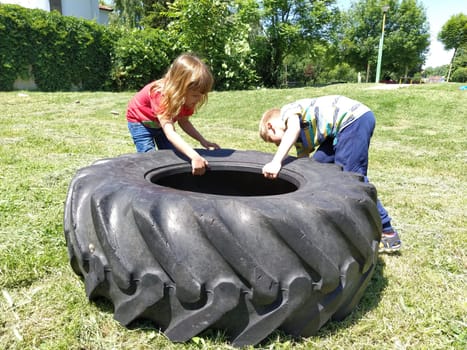Sremska Mitrovica, Serbia, May 20, 2020. Children play and pick up the tire. Car parts and accessories in a kid's game. A boy and a girl 6 and 7 years old are doing strength exercises on the grass.