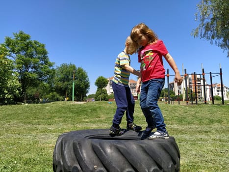 Sremska Mitrovica, Serbia, June 6, 2020. Children jump on the tire from the wheel. A boy and a girl stand on a rubber tire and try to rock it. Outdoor sports.