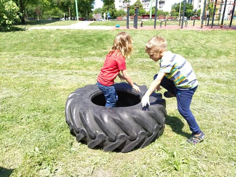Sremska Mitrovica, Serbia, May 20, 2020. Children play and pick up the tire. Car parts and accessories in a kid's game. A boy and a girl 6 and 7 years old are doing strength exercises on the grass.