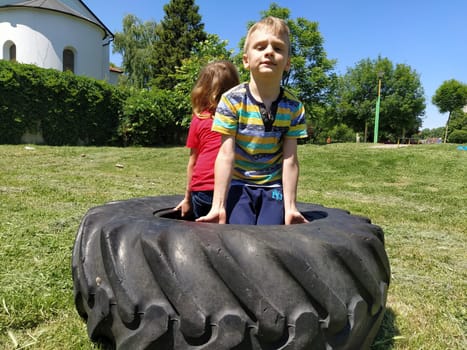 Sremska Mitrovica, Serbia, May 20, 2020. Children play and pick up the tire. Car parts and accessories in a kid's game. A boy and a girl 6 and 7 years old are doing strength exercises on the grass.