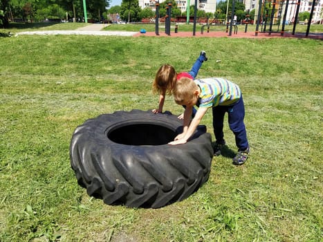 Sremska Mitrovica, Serbia, May 20, 2020. Children play and pick up the tire. Car parts and accessories in a kid's game. A boy and a girl 6 and 7 years old are doing strength exercises on the grass.