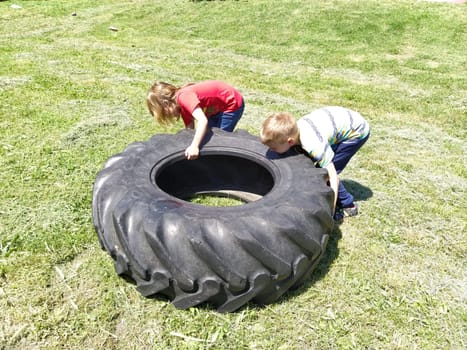 Sremska Mitrovica, Serbia, May 20, 2020. Children play and pick up the tire. Car parts and accessories in a kid's game. A boy and a girl 6 and 7 years old are doing strength exercises on the grass.