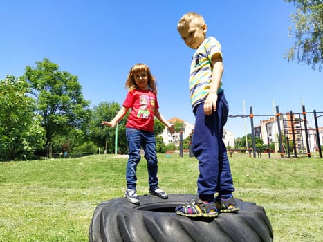Sremska Mitrovica, Serbia, June 6, 2020. Children jump on the tire from the wheel. A boy and a girl stand on a rubber tire and try to rock it. Outdoor sports.