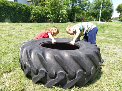 Sremska Mitrovica, Serbia, May 20, 2020. Children play and pick up the tire. Car parts and accessories in a kid's game. A boy and a girl 6 and 7 years old are doing strength exercises on the grass.
