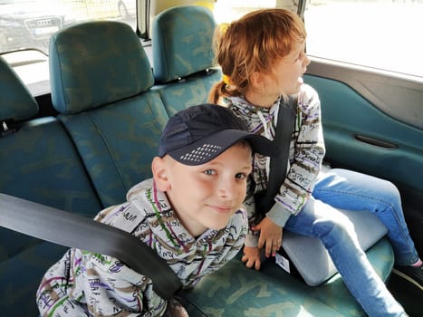 Belgrade, Serbia. 06 June 2020. Children in the car. A boy and a girl are sitting in the back seat, laughing and grimacing. Children fasten their seat belts. A child in a cap. Children - twins of different faces dressed in the same clothes