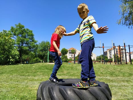 Sremska Mitrovica, Serbia, June 6, 2020. Children jump on the tire from the wheel. A boy and a girl stand on a rubber tire and try to rock it. Outdoor sports.