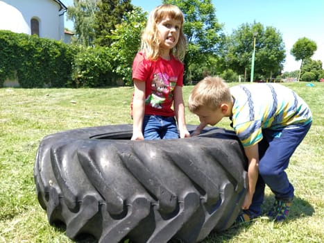 Sremska Mitrovica, Serbia, May 20, 2020. Children play and pick up the tire. Car parts and accessories in a kid's game. A boy and a girl 6 and 7 years old are doing strength exercises on the grass.