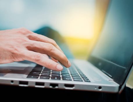 Close-up of a man's hands working on his laptop. Side view of hands working on laptop, Close up of a person's hands on the laptop keyboard outdoors, Close up of fingers on laptop keyboard