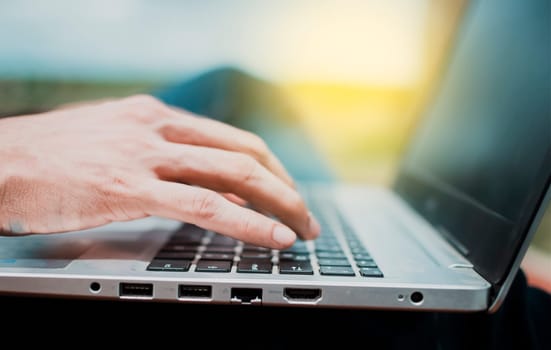 Close up of a person's hands on the laptop keyboard outdoors, Close-up of a man's hands working on his laptop. Side view of hands working on laptop