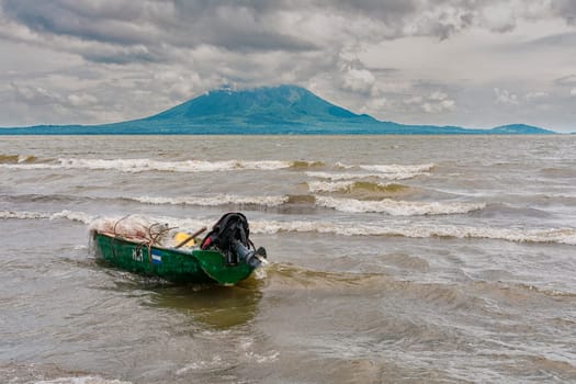 A wooden fishing boat on the shore of a lake, Nicaragua. Fishing boat on the shore of a lake, A fishing boat on the shore of a lake with volcanoes in the background