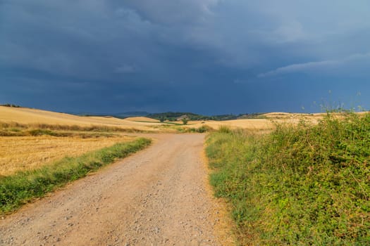 Rural road in the Spanish countryside among agricultural fields, after wheat harvest season. Navarra, Spain