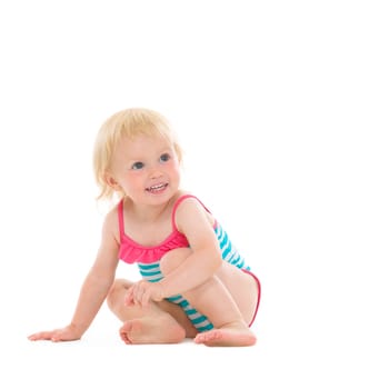 Curious baby in swimsuit sitting on floor and looking on copy space