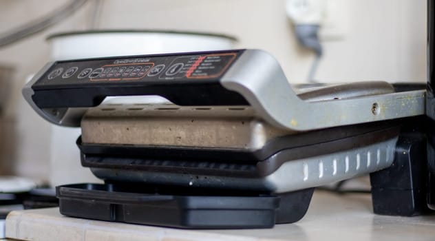 Dirty electric grill with a closed lid. Dirty electric stove in the home kitchen. Appliance for cooking at home. Made of stainless steel, has a special non-stick coating