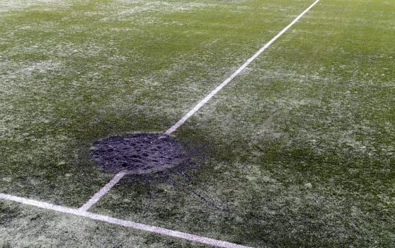 A hole in the ground from a cannon shell explosion filled with fresh earth at a football stadium. Shelling crater in the city. Playground. War in Ukraine. Destruction of civilian infrastructure