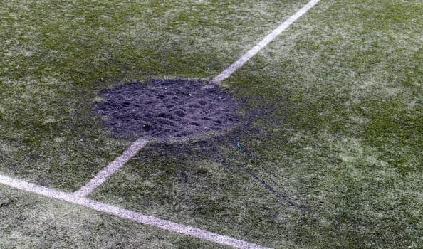 A hole in the ground from a cannon shell explosion filled with fresh earth at a football stadium. Shelling crater in the city. Playground. War in Ukraine. Destruction of civilian infrastructure