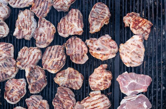 top view closeup of pork slices being grilled on black iron barbeque grate outdoors