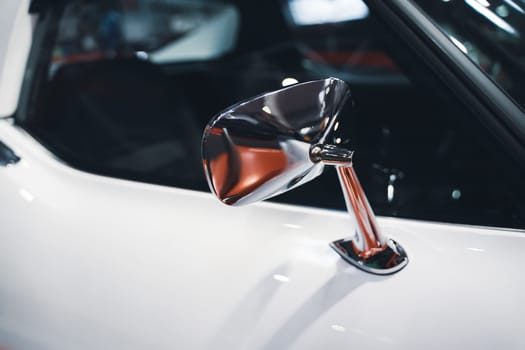 side view detail closeup of chrome rear mirror on white car with classic vintage design