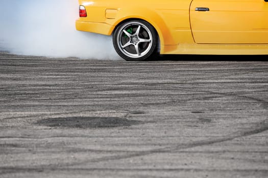 closeup side view of yellow sport car drifting on gray speed tarmac track with white smoke coming out of the back tire wheel with copy space available